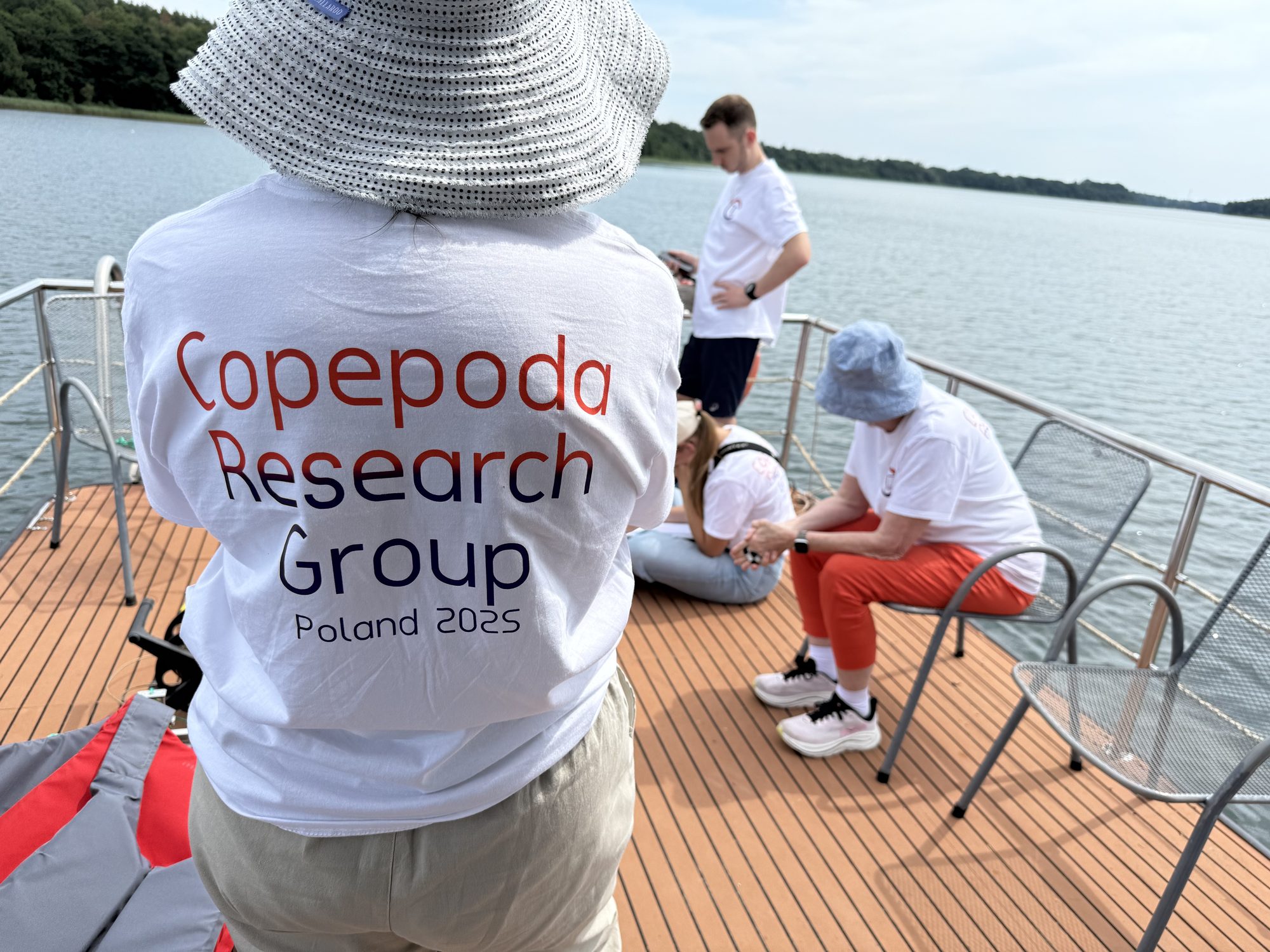 Researchers on a boat deck sorting plankton samples, one wearing a Copepoda Research Group Poland 2025 shirt