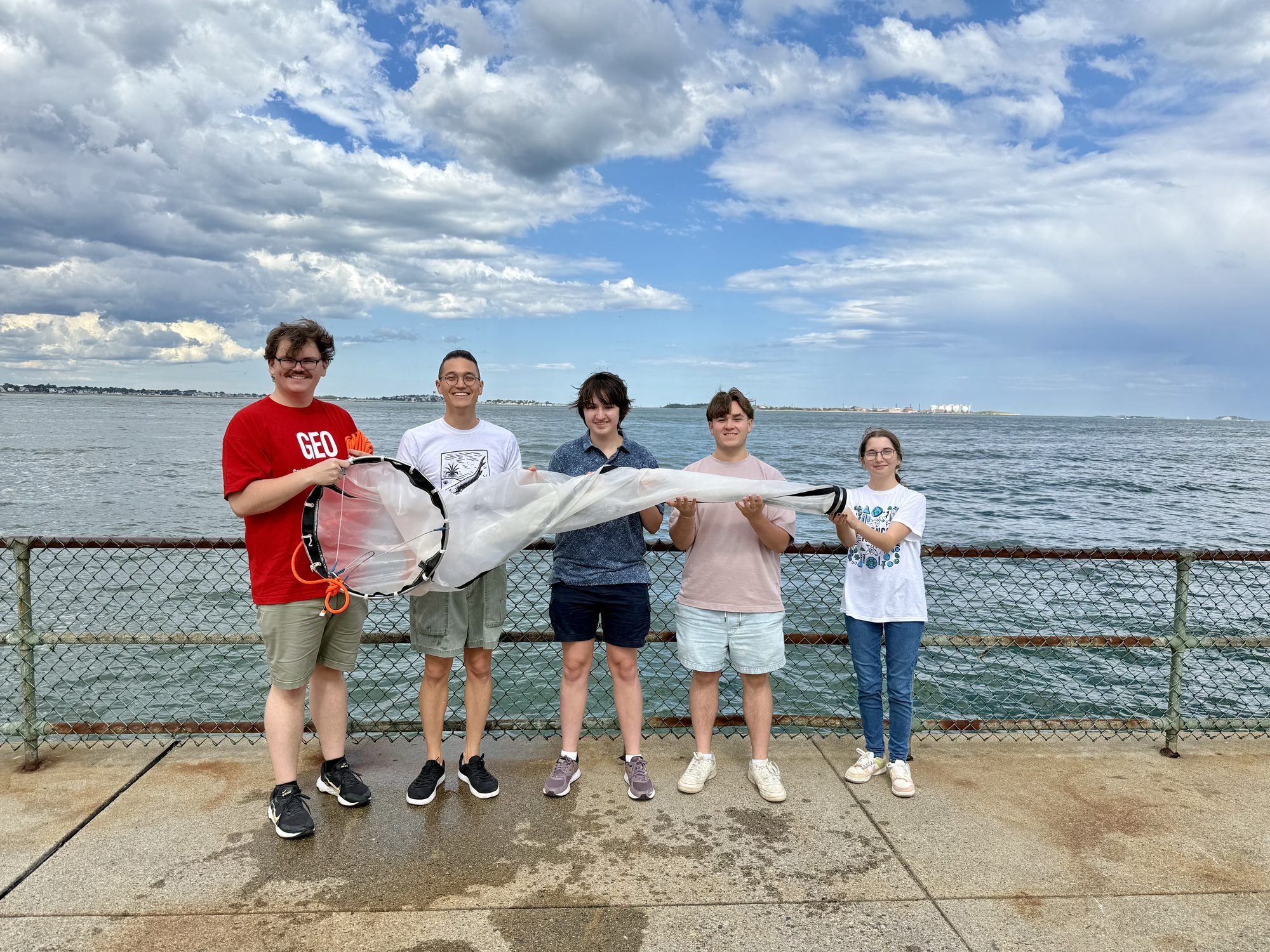 ZEAL lab members holding a plankton net on a waterfront pier